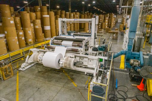 Many rolls of paper stacked up in the Roosevelt plant. Machine producing paper rolls.